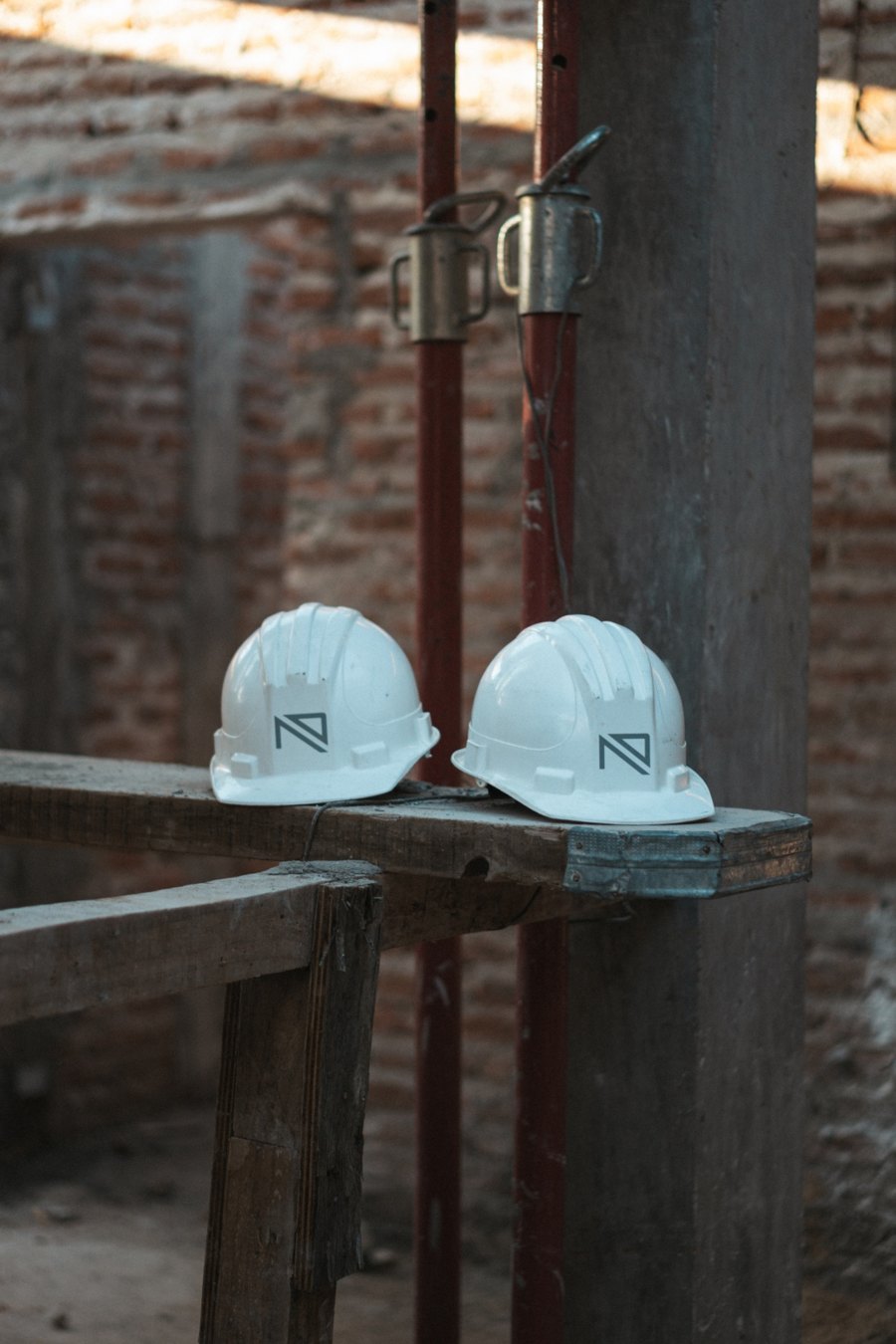 Dos cascos blancos con el logo del estudio apoyados en un tablón de obra